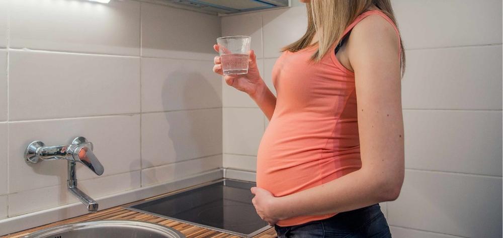 A pregnant woman in the summer heat, holding a glass of water in the kitchen