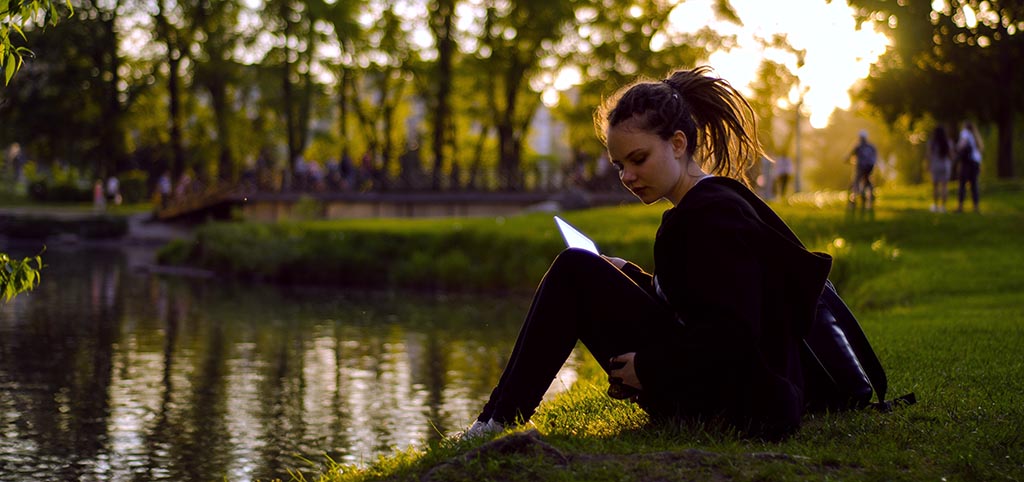A girl is seated in front of a pond in a urban park